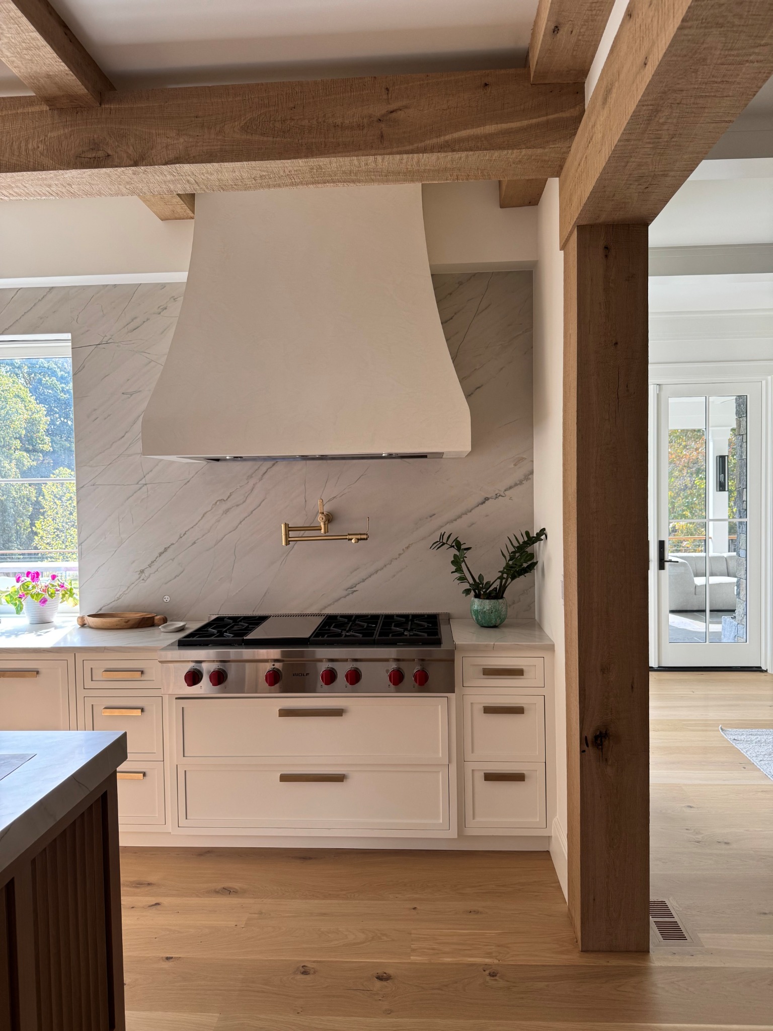 Custom kitchen with painted cabinetry, natural wood beams, stone backsplash, and range hood